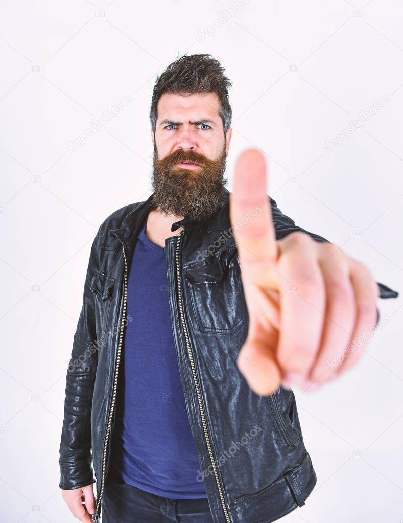 Man with beard and mustache on strict face shows index finger gesture, pointing, close up. Menswear and fashion concept. Macho, bearded hipster wears leather jacket, white background