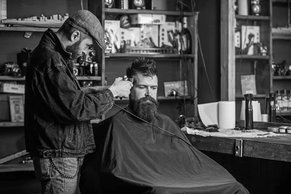Barber with clipper trimming hair on temple of bearded client. Barber with hair clipper work on hairstyle for hipster, barbershop background. Hipster lifestyle concept. Hipster client getting haircut — Stock Photo, Image