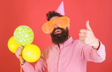 Sakal ve bıyık mutlu yüz tutan grup hava balonları, kırmızı arka plan üzerinde olan adam. Kutlama kavramı. Hippi dev güneş gözlüğü Doğum günü kutluyor. Parti şapkalı adamı yukarı hareketi gösterir