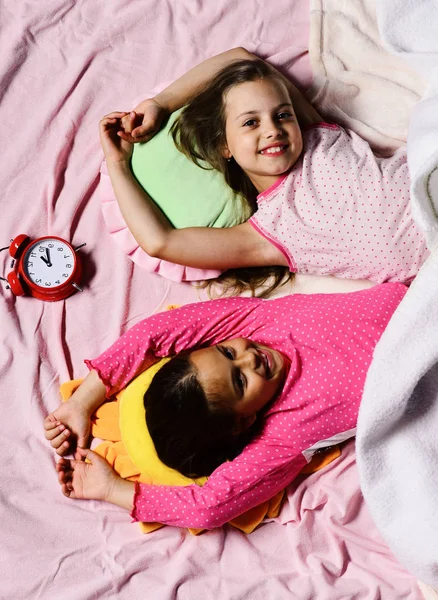 Schoolgirls in pink pajamas wallow on colorful pillows, top view