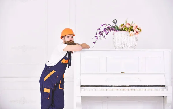 Tipo reflexivo apoyado en la parte superior del piano blanco vintage con jarrón de flores de vidrio aislado sobre fondo blanco. Trabajador barbudo disfrutando de un breve descanso — Foto de Stock