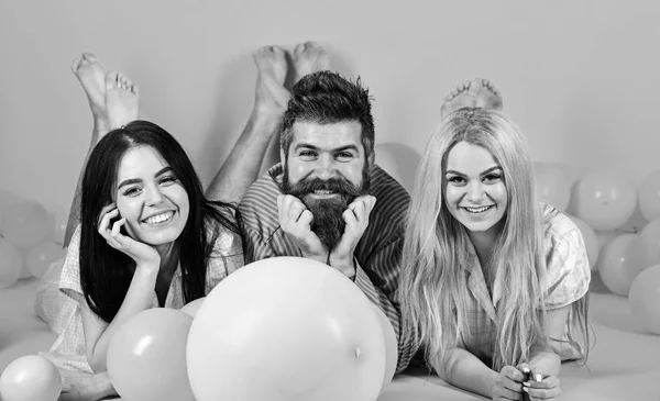 Loira e morena em rostos sorridentes se divertir com macho barbudo. Melhores amigos, amantes perto de balões, fundo rosa. Amantes ou melhores amigos de pijama na festa do quarto feminino. Conceito de Gossip — Fotografia de Stock