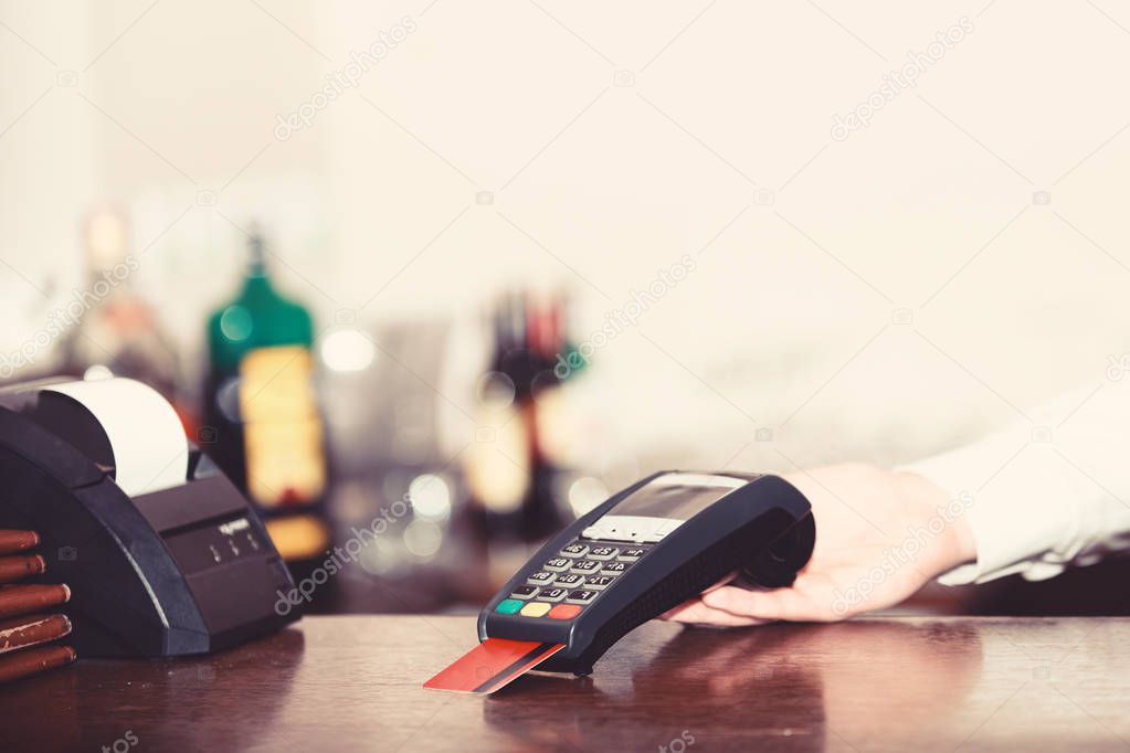 Cashiers hand holds credit card reader on light defocused background.