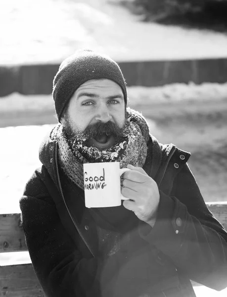 Heyecanlı adam, sakal ve bıyık sakallı hippi beyaz Don içecekler Kupası ile Günaydın karlı kış günü açık havada doğal adam tahta bankta oturan metin kaplı — Stok fotoğraf