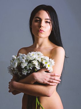 Sağlıklı ciltle pürüzsüz kadınla çekici görünüyor. Doğal kozmetik kavramı. Sakin yüz çıplak kız papatya çiçeği göğüsler önünde tutar. Bayan göğüsler çiçeklerle, gri arka plan kapsar