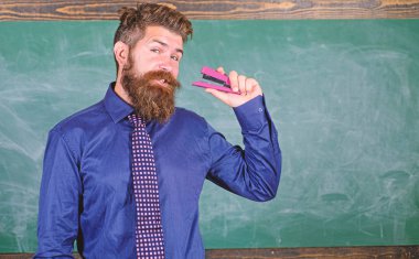 Sakallı adam öğretmen veya eğitimci formal giyim zımba kara tahta arka plan tutar. Okul malzemeleri ve Kırtasiye. Zımba güvenli bir şekilde kullanmak. Tehlikeli ileti örneği olarak zımba ile dikkatli olun