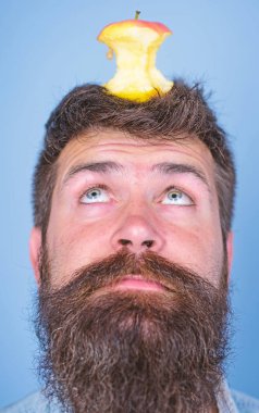 Adam yakışıklı hipster uzun sakal neredeyse kafasına elma güdük hedef olarak yem. Canlı hedef kavramı. Hipster sürpriz elma güdük hedef üzerinde kafa mavi arka plan, yüz kadar yakın. Kilo kaybı gol