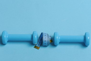 Plastikten yapılmış dambıllar ve cyan arkaplanda ölçüm bandı