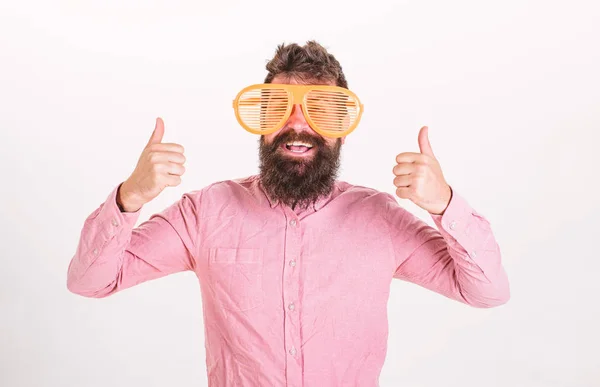 Gute-Laune-Konzept. Hipster blicken durch eine riesige gestreifte Sonnenbrille. Mann mit Bart zeigt Daumen hoch. Mann mit Bart und Schnurrbart auf glücklichem Gesicht trägt lustige große Brille, weißer Hintergrund — Stockfoto