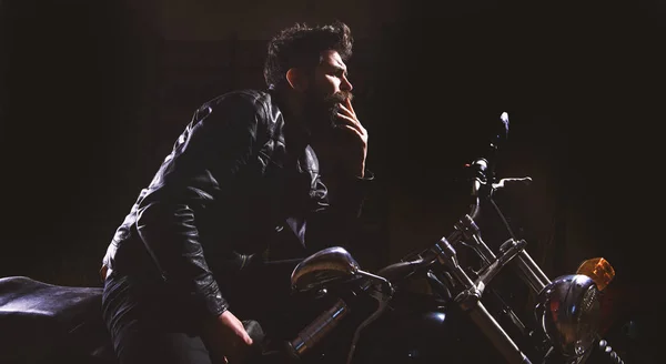 Nat racer koncept. Mand med skæg, biker i læderjakke sidder på motorcykel i mørke, sort baggrund. Macho, brutal biker i læderjakke ridning motorcykel om natten, kopiplads - Stock-foto