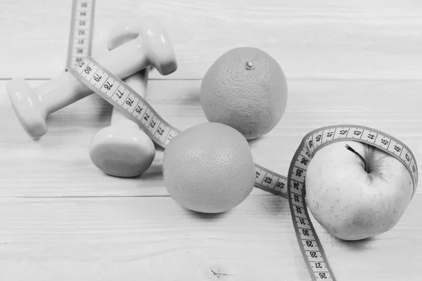 Concepto de ejercicio, peso de mancuernas con cinta métrica, naranja y manzana — Foto de Stock
