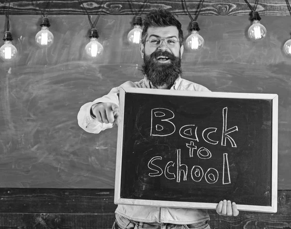 Professeur de lunettes tient tableau noir avec inscription de retour à l'école. Retour à l'école. Homme avec barbe et moustache sur le visage heureux invite les étudiants, pointant vers l'avant, tableau sur fond — Photo