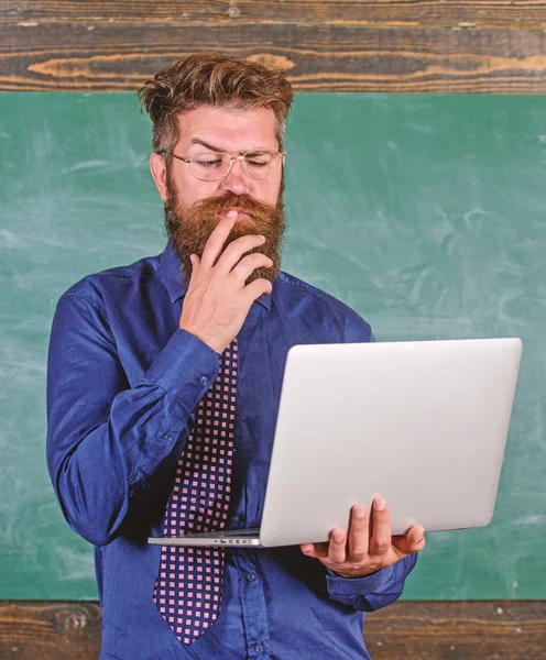 Concepto de educación a distancia. Navegar por Internet. Hipster profesor usar gafas y corbata sostiene portátil navegar por Internet. Profesor barbudo hombre con portátil moderno navegar por internet pizarra fondo — Foto de Stock