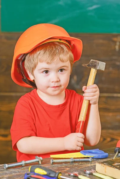 Un gosse en casque orange tenant un marteau dans ses mains. Cours d'artisanat à la maternelle. Portrait de petit garçon en atelier — Photo