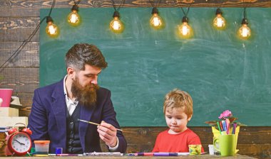 Çocuk ve meşgul yüz boyama, resim öğretmeni. Sakallı öğretmeni, sınıfta, kara tahta arka plan çizmek için küçük oğlu baba öğretir. Sanat ders kavramı. Yetenekli sanatçı oğlumla vakit geçirmek