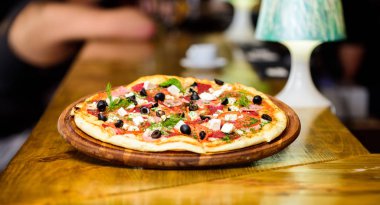 Pizza restoran. İtalyan pizza kavramı. Ahşap tahta plaka üzerinde lezzetli sıcak pizza. Gıda teslim Servisi. Pizza dereotu ile servis. Pizza domates siyah zeytin ve jambon. Gıda kavramı götürün