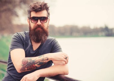 Nehir setin arka plan üzerinde giyer gözlüklü, sakal ve bıyıklı adam. Hippi moda güneş gözlüğü ile kendine güvenen yüzünde. Adam ile şık güneş gözlüğü kendinden emin görünüyor. Erkek moda kavramı