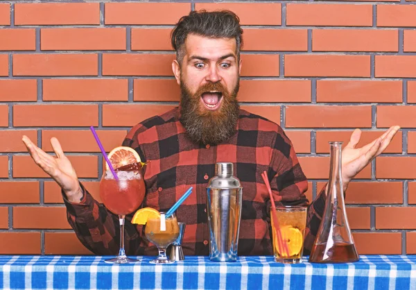 Alcoholic drinks concept. Man in checkered shirt on brick wall background prepares drinks. Barman with long beard and mustache and stylish hair on excited face ready to make alcoholic cocktail