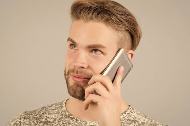 Adam düşünceli rüya gibi kullanım akıllı telefon iletişim, gri arka plan. İletişim kavramı. Adam çekici de sakal ve saç modeli konuşmak Smartphone ile bakımlı. Mobil konuşmayı adam