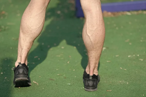 Pies en zapatos deportivos negros sobre hierba verde. Piernas musculares con venas en el estadio o arena en el exterior soleado. Salud y estilo de vida saludable. Entrenamiento deportivo y entrenamiento — Foto de Stock