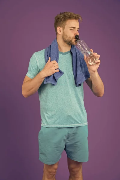 L'homme boit de l'eau après l'entraînement sur fond violet. Sportif assoiffé avec bouteille en plastique sur fond violet. Soif et déshydratation. Eau potable pour la santé. Activité sportive et énergie — Photo