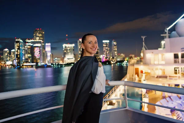 Mujer de negocios sonríe a bordo de un barco por la noche en Miami, EE.UU. Mujer sensual en chaqueta de traje en el horizonte de la ciudad. Moda, belleza, mira. Viajar por negocios. Lujuria, aventura, descubrimiento, viaje — Foto de Stock