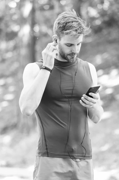 Music best companion to run. Man athlete on busy face set up play list, nature background. Sportsman training headphones listen music. Athlete with bristle with fitness tracker or pedometer