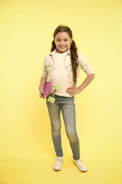 A los niños les gusta patinar. Alegre y feliz. Niña estilo casual con penny board disfrutar de la infancia. Chica alegre feliz con el fondo amarillo monopatín. Hobby y concepto de ocio — Foto de Stock