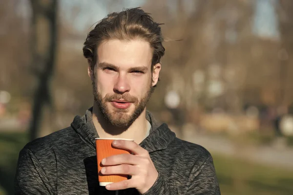 Bearded man with takeaway drink on fresh air. Macho hold disposable coffee cup in sunny park. Coffee or tea mood. Drink and food outdoor. Morning tea for breakfast