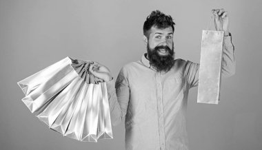Mutlu yüz ve modaya uygun sakal alışveriş torbaları tutan adam. Alışverişkoliğin tüm maaş giysileri üzerinde harcama. Üzerinde mavi arka plan izole pembe gömlekli sakallı adam. Alışveriş zevk hipster sakallı