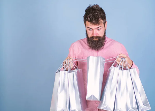 Man with trendy beard and mustache isolated on blue background. Hipster in pink shirt with surprised face holding silver bags. Bearded man shocked with his purchase, sales and shopping concept — Stock Photo, Image