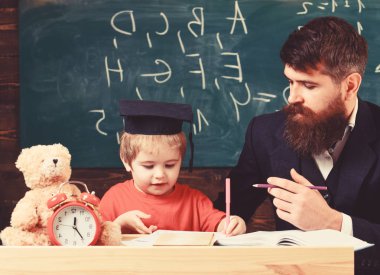 Öğretmen ve öğrenci kolej, kara tahta arka plan içinde. Çocuk çalışmaları dikkatle dinlerken öğretmen ile. İlköğretim kavramı. Baba oğul öğretir temel bilgi, tartışmak, açıklamak