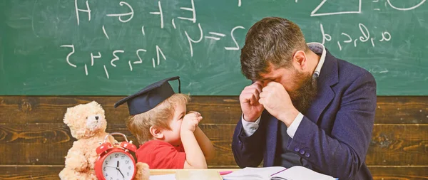 Kid cheerful boxing, beating dad. Playful child concept. Teacher and pupil in mortarboard, chalkboard on background. Father with beard, teacher teaches son, little boy, while child beating him