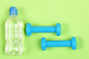 Yeşil dalgalı arkaplanda siyan plastikten yapılmış dambıllar.