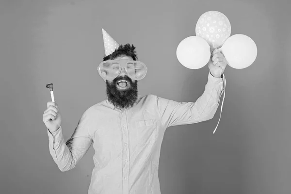 Homem com barba e bigode na cara feliz segura balões de ar, fundo azul. Hipster em óculos gigantes comemorando aniversário. O tipo de chapéu de festa com atributos de férias celebra. Conceito de partido — Fotografia de Stock