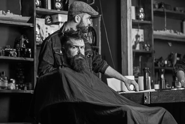 Sakallı adam kesme makinesi sınıf değiştirme Kuaför bekleyen siyah pelerin ile kaplı. Hipster istemci Başlarken saç kesimi. İstemci ile sakal düzeltme veya bakım için hazır. Saç kesimi işlem kavramı