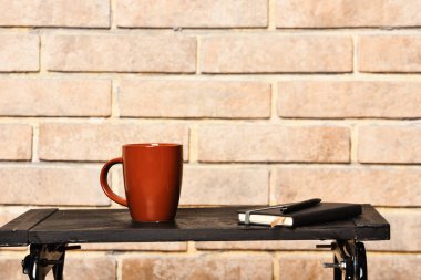 Cup of hot beverage and notebook on small table. clipart