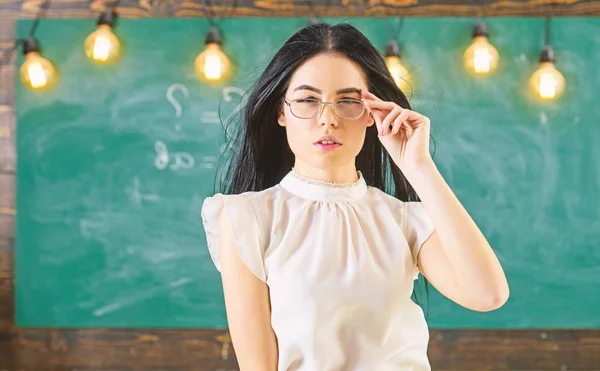 Vrouw met lange haren in witte blouse staat in de klas. Strenge leraar concept. Leraar met glazen en wapperende haren ziet er aantrekkelijk uit. De strenge leraar Lady op kalme gezicht staat voor schoolbord — Stockfoto