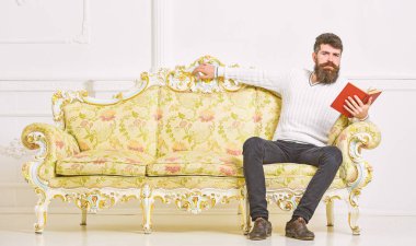 Kendi eğitim kavramı. Maço kitap okumak, eğitim sakin yüz. Sakal ve bıyık oturur barok tarzı kanepe, tutar kitap, beyaz duvar arka plan üzerinde olan adam. Adam okuma kitabı oturma odasında