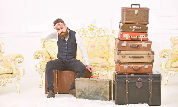 Macho elegant mit strenger Miene sitzt müde neben einem Stapel Vintage-Koffer. Mann, Butler mit Bart und Schnurrbart liefert Gepäck, luxuriöser weißer Innenraum. Gepäck- und Umzugskonzept — Stockfoto