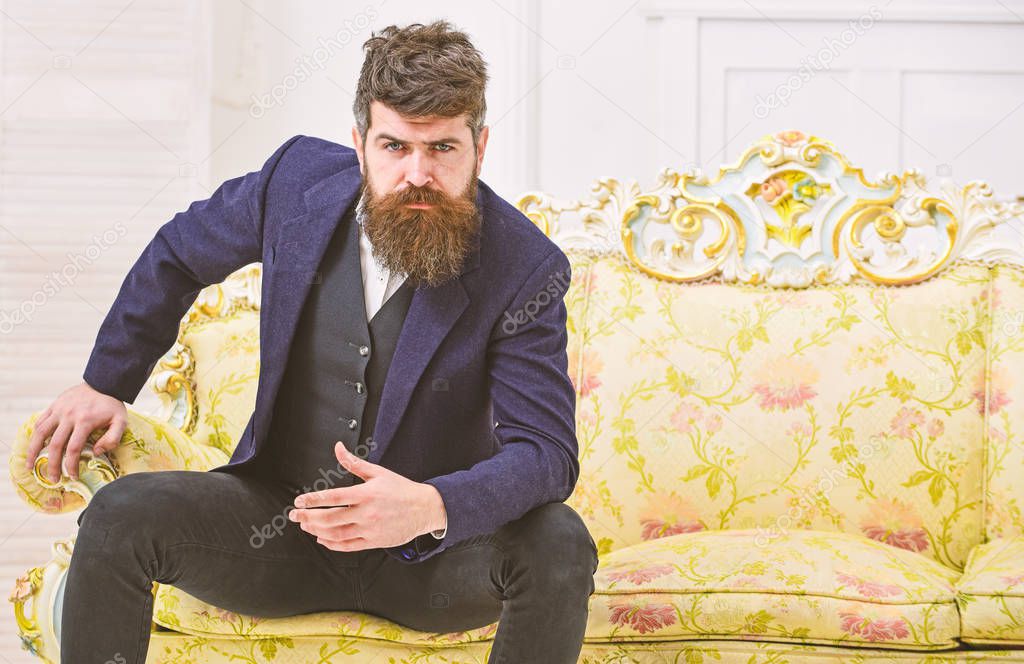 Fashion and style concept. Man with beard and mustache wearing classic suit, stylish fashionable outfit. Macho attractive and elegant on serious, thoughtful face sitting on old fashioned luxury sofa