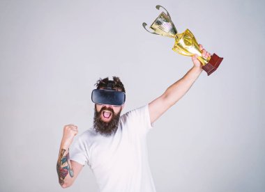 Sanal başarı kavramı. Hipster mutlu yüz üzerinde sanal şampiyonluğa ulaştı. Vr bardaklarda sakallı adam kazanan, gri arka plan var. Şampiyonluğa ulaştı, Vr gözlüklü tutun el altın kadehi