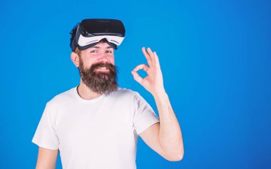 Adam uzun sakallı ve Ok jest gösterilen mutlu yüzünde geniş bir gülümseme ile. Sakallı enginner Vr kulaklık, dijital ilerleme kavramı, yeni modeli sınama. Üzerinde mavi arka plan izole trendy sakallı hippi