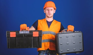 İşçi, repairer, tamirci, Oluşturucu düşünceli yüzündeki iş için ekipman seçimi. Kask, kask içinde adam araç kutusu ve araç, mavi arka plan ile bavul tutar. Araç kutusu ve ekipman kavramı