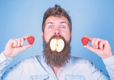 Meyve doldurma. Adam yakışıklı hipster uzun sakal elma tutun çilek yiyin. Hipster sürpriz doldurma meyve tadını çıkarın. Adam doldurulmuş elma. Apple ağız sakallı hippi çilek her iki elinde tutar.