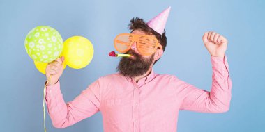 Doğum günü kap ve dans, büyük deli gözlük parti sert, eğlenceli zaman kavramı sakallı adam. Hipster kesilmiş sakal ve bıyık parti düdük ve mavi arka plan üzerinde parlak balonlar ile poz ile