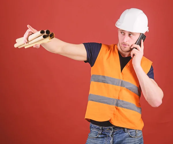 Onderhandelingen concept. Ingenieur, architect, bouwer op drukke gezicht spreekt op smartphone terwijl bezit blauwdrukken, kopie ruimte. Man, architect in helm houdt toezicht op de bouw van telefoon, rode achtergrond — Stockfoto