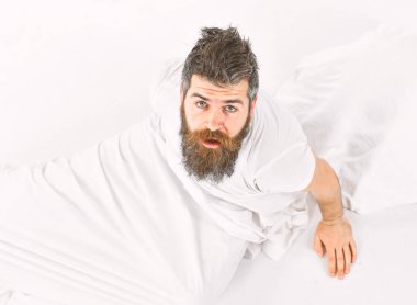 Uykulu yüz adamla oturup yatakta, beyaz çarşaf