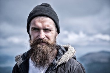 Man with long beard and mustache wears hat. Hipster on strict face with beard looks brutally while hiking. Masculinity concept. Man with brutal bearded appearance, brutal unshaven man looks untidy clipart