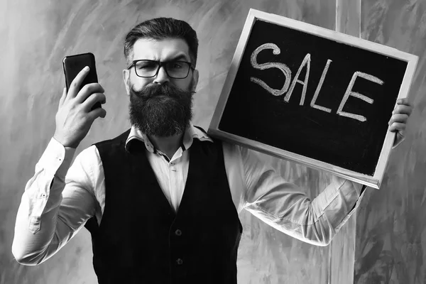 满嘴胡子的男人，残忍的高加索嬉皮士，带着智能手机的销售题词 — 图库照片
